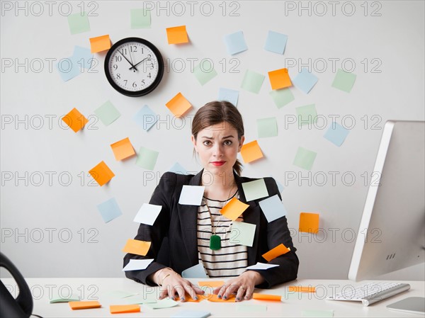 Studio shot of young woman working in office covered with adhesive notes. Photo : Jessica Peterson