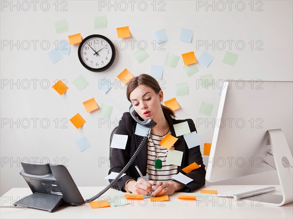 Studio shot of young woman working in office covered with adhesive notes. Photo: Jessica Peterson