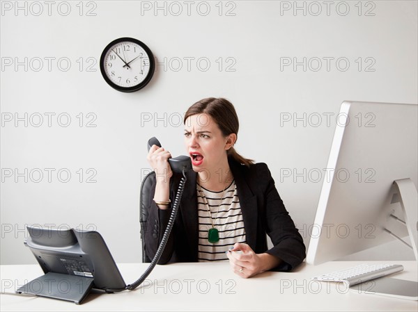 Studio shot of young woman working in office yelling into phone. Photo : Jessica Peterson