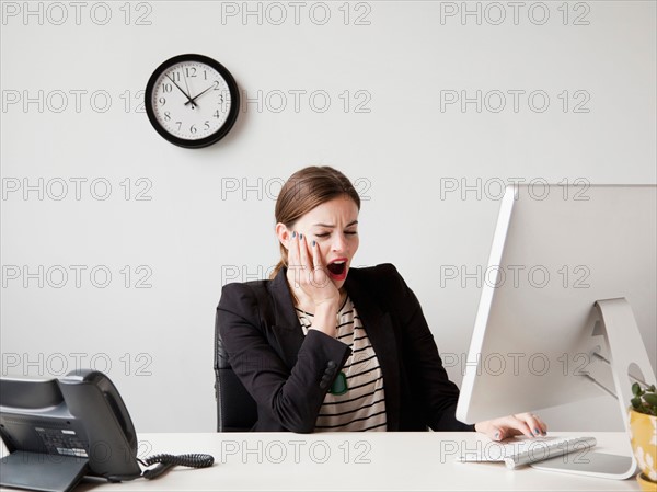 Studio shot of young woman working in office yawning. Photo: Jessica Peterson