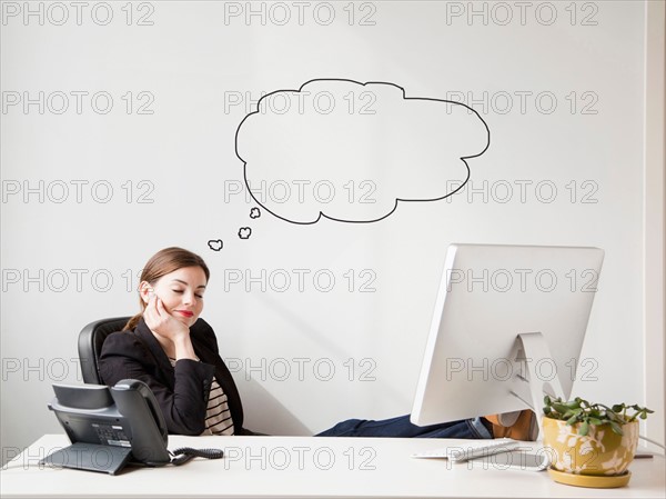Studio shot of young woman working at desk with thought bubbles next to her head. Photo : Jessica Peterson