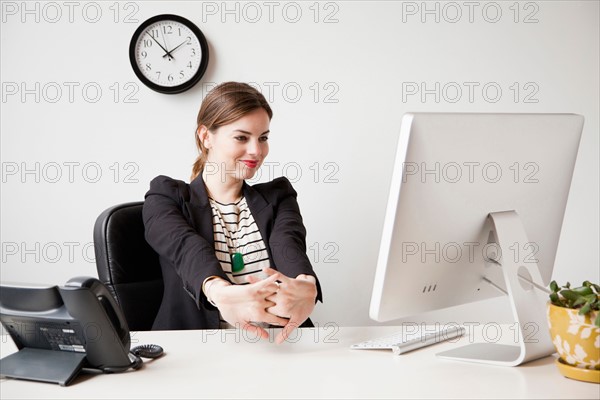 Studio shot of young woman working in office and stretching her arms. Photo: Jessica Peterson