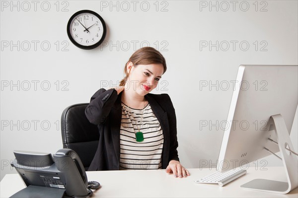 Studio shot of young woman working in office and touching her neck. Photo: Jessica Peterson