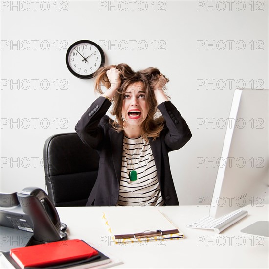 Studio shot of young woman working in office and tearing her hair out. Photo : Jessica Peterson