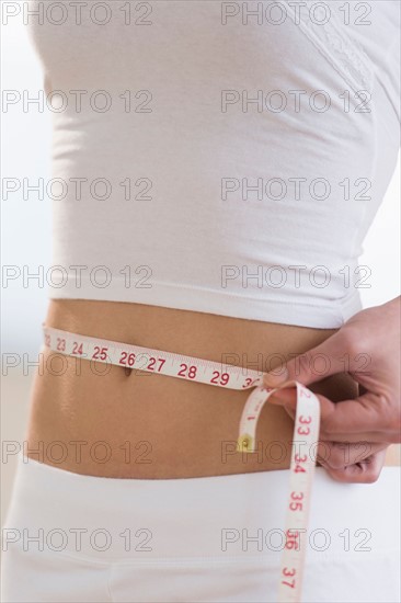 Midsection of woman measuring waistline.