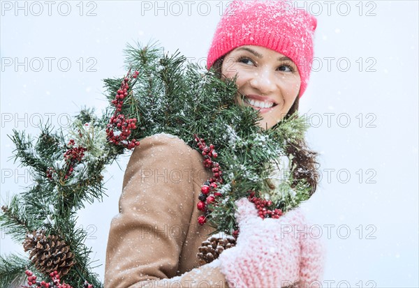 Portrait of woman in winter clothes carrying wreath.