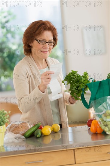 Senior woman reading shopping list in kitchen.