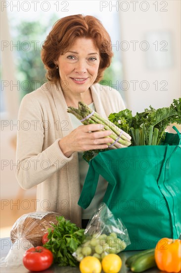 Senior woman with groceries in kitchen.