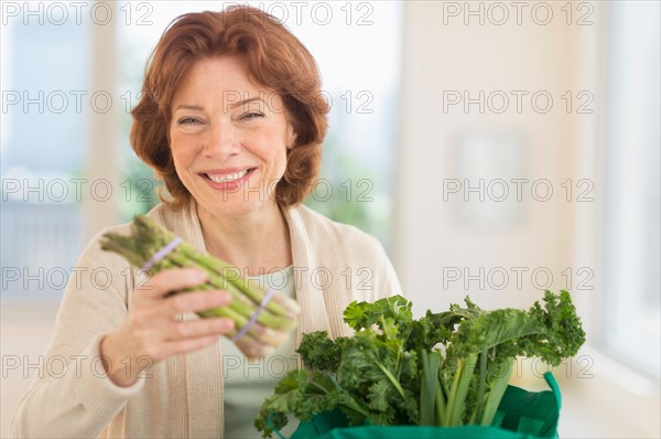Senior woman with groceries in kitchen.