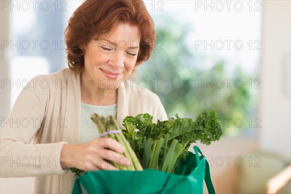 Senior woman with groceries in kitchen.