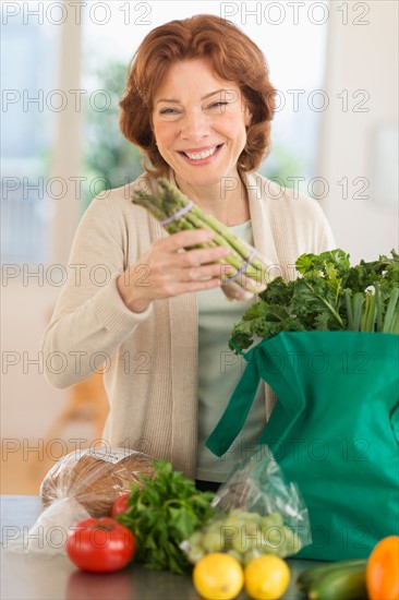 Senior woman with groceries in kitchen.