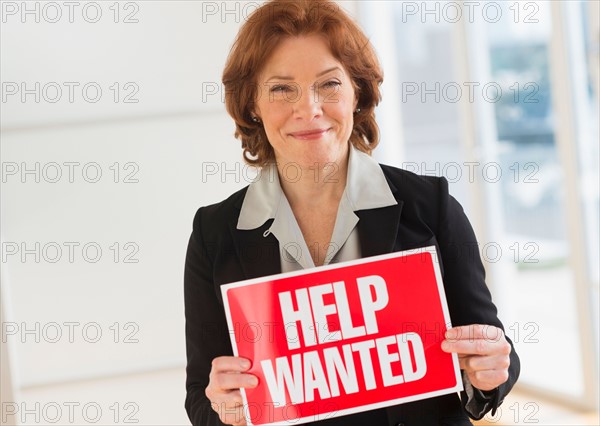 Portrait of businesswoman holding help wanted sign.