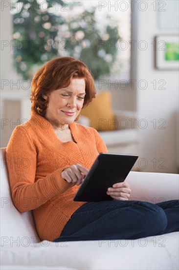 Woman sitting on sofa using digital tablet.