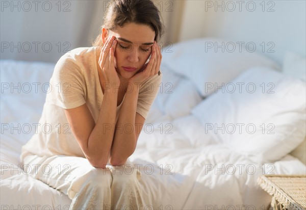 Young woman sitting on bed with headache.