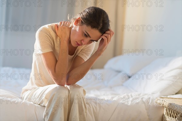 Young woman sitting on bed with headache.