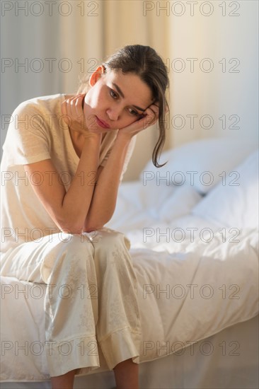 Young woman sitting on bed with headache.