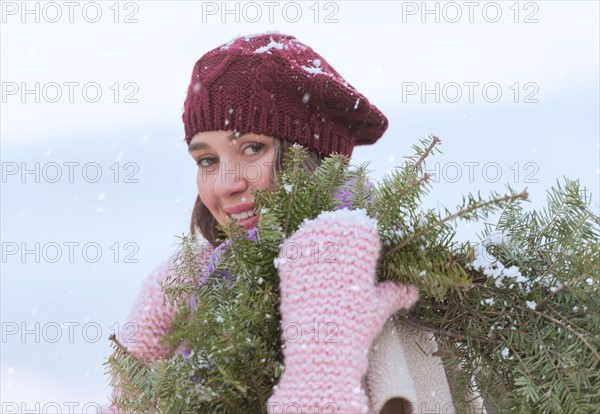 Portrait of young woman wearing knit hat, gloves and scarf an carrying fir wreath.