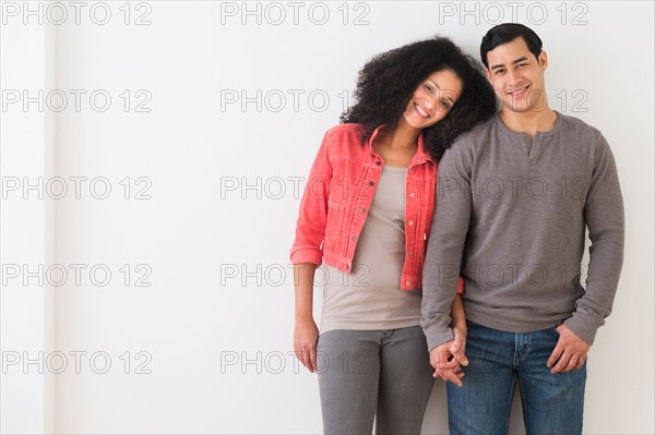 Portrait of smiling couple standing against white wall.