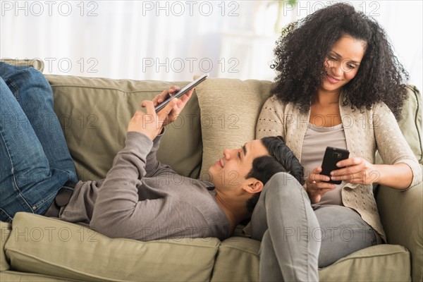 Couple using digital tablet and mobile phone on sofa.