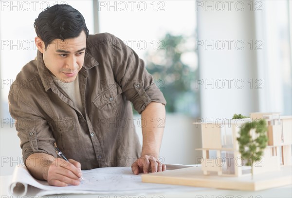 Male architect working with blueprint and model home.