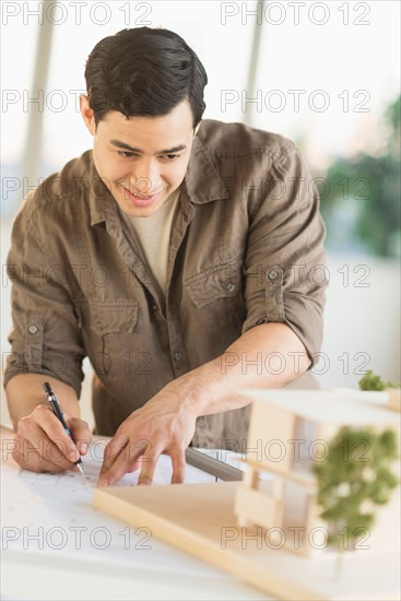 Male architect working with blueprint and model home.