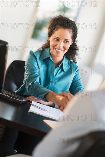 Woman shaking hand with man at desk.