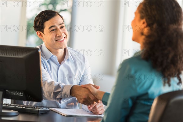 Woman shaking hand with man at desk.