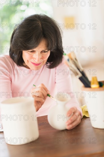 Senior woman painting handmade pottery.