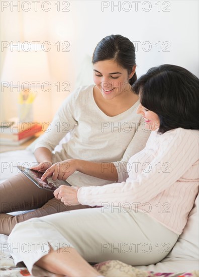 Grandmother and granddaughter (16-17) lying on bed with digital tablet.