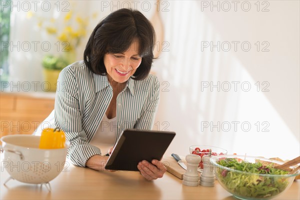 Senior woman holding digital tablet while preparing salad .