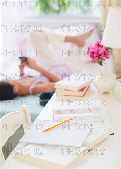 View of Teenage girl ( 16-17 years) using mobile phone next to desk with books