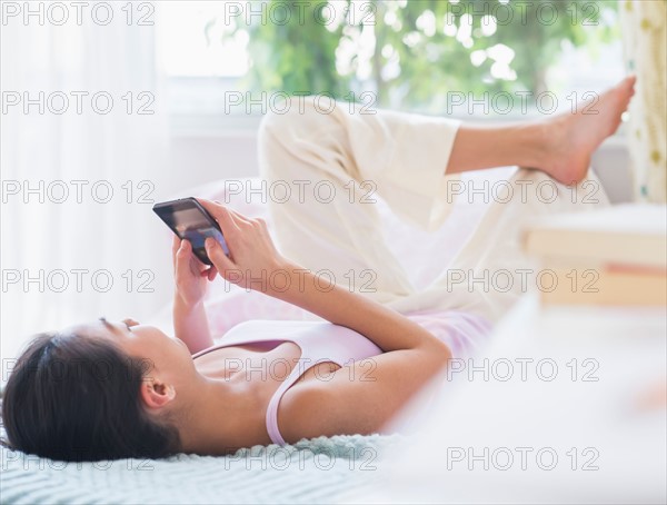 View of Teenage girl ( 16-17 years) using mobile phone lying on bed