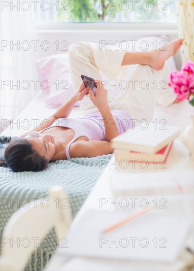 View of Teenage girl (16-17 years) using mobile phone next to desk with books