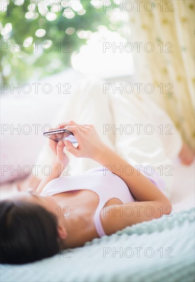 View of Teenage girl (16-17 years) using mobile phone lying on bed