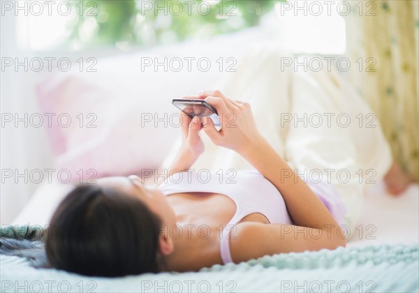 View of Teenage girl ( 16-17 years) using mobile phone lying on bed