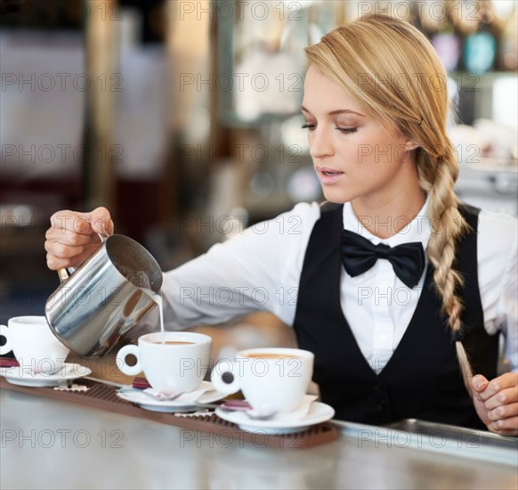 Female barista pouring milk into coffee cup