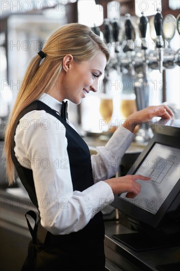 Young waitress using computer at restaurant counter