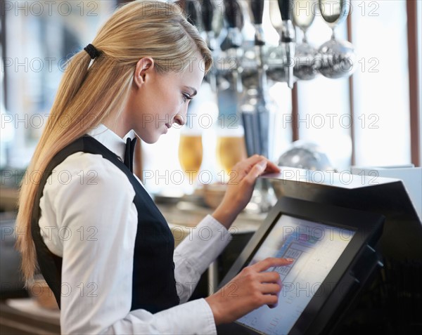 Young waitress using computer at restaurant counter