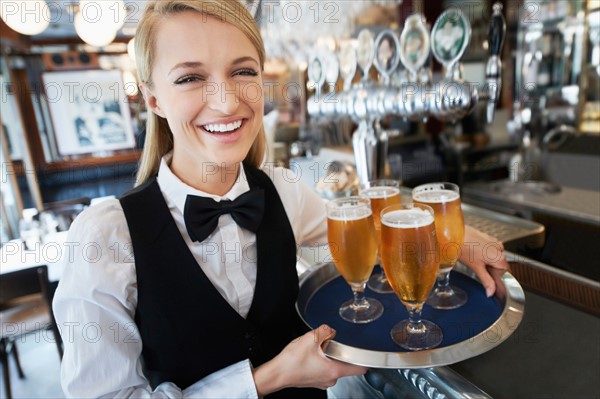 Portrait of young woman holding tray with beer glasses