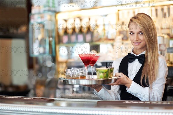 Portrait of female bartender holding tray with cocktails