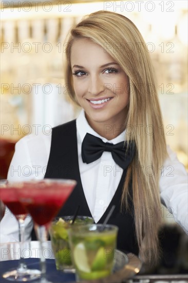 Portrait of female bartender holding tray with cocktails