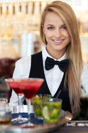 Portrait of female bartender holding tray with cocktails