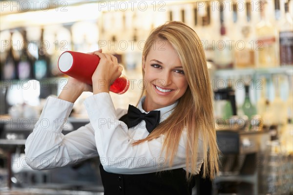 Young female bartender using cocktail shaker