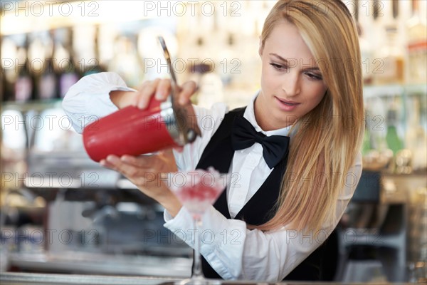 Young female bartender pouring cocktail