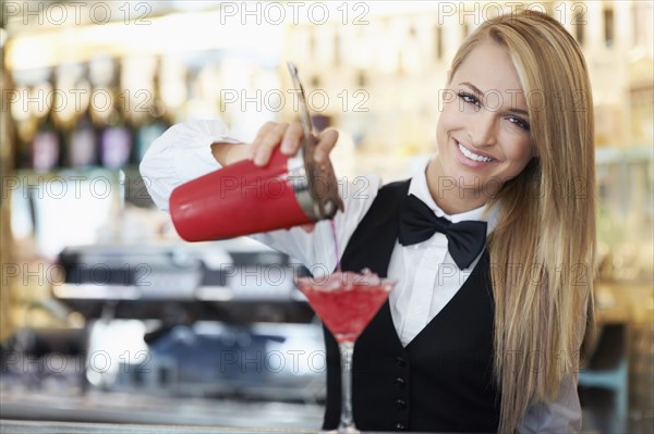 Young female bartender pouring cocktail