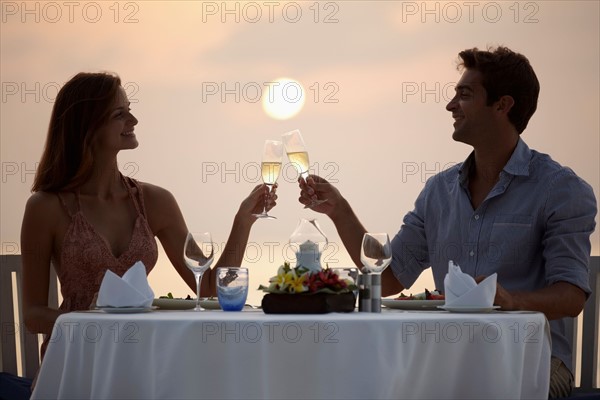 Couple at table on beach, toasting
