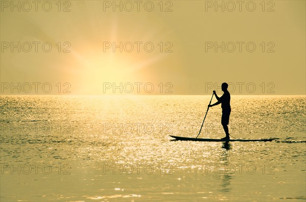 Man standing on paddle board at sunset