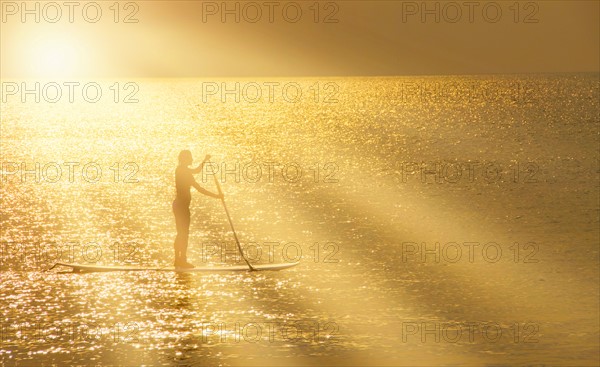 Man standing on paddle board at sunset