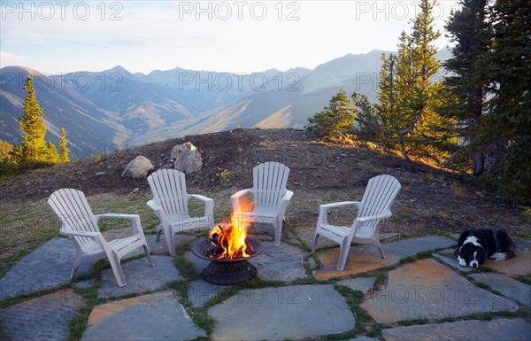 Dog lying down by fire pit and four empty chairs