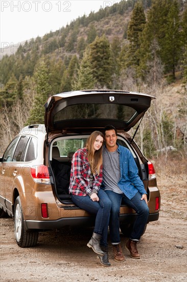 Portrait of young couple sitting in car trunk in non-urban scene